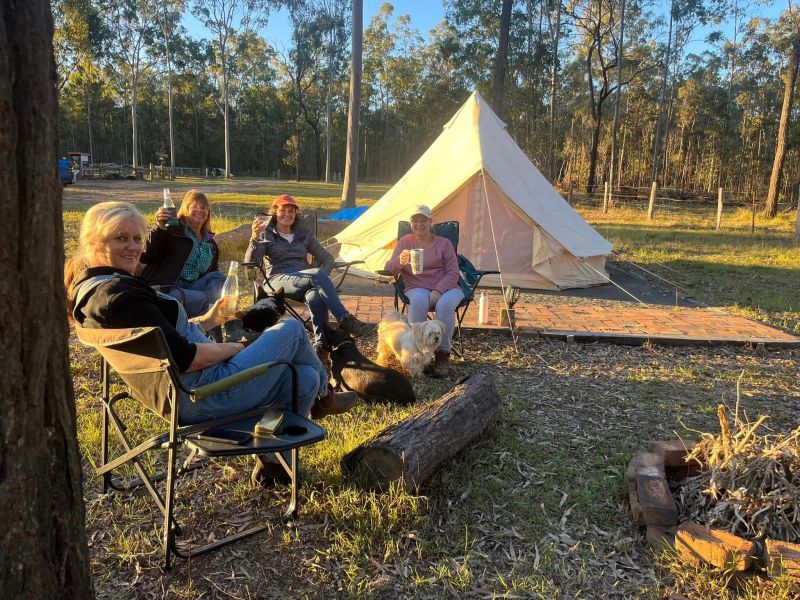 a group of women sitting around having a drink in front of a tent