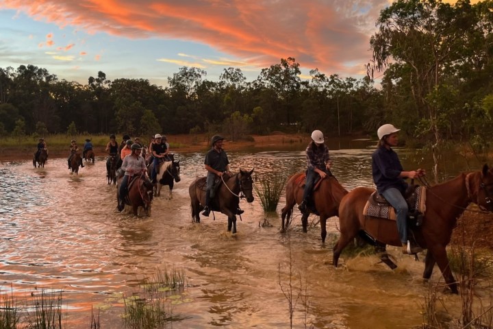 a group of people riding horses through the water